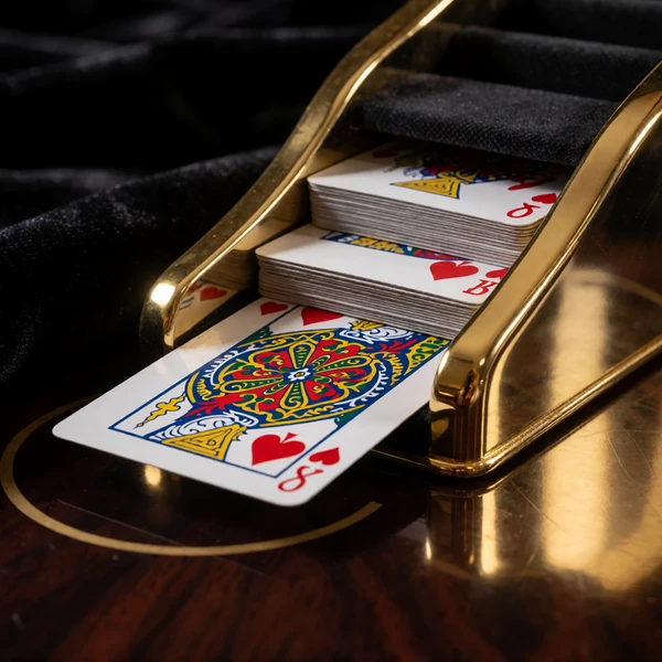 Baccarat-Kartenschlitten mit Goldverzierung auf dunklem Spieltisch im Millioner Live Casino